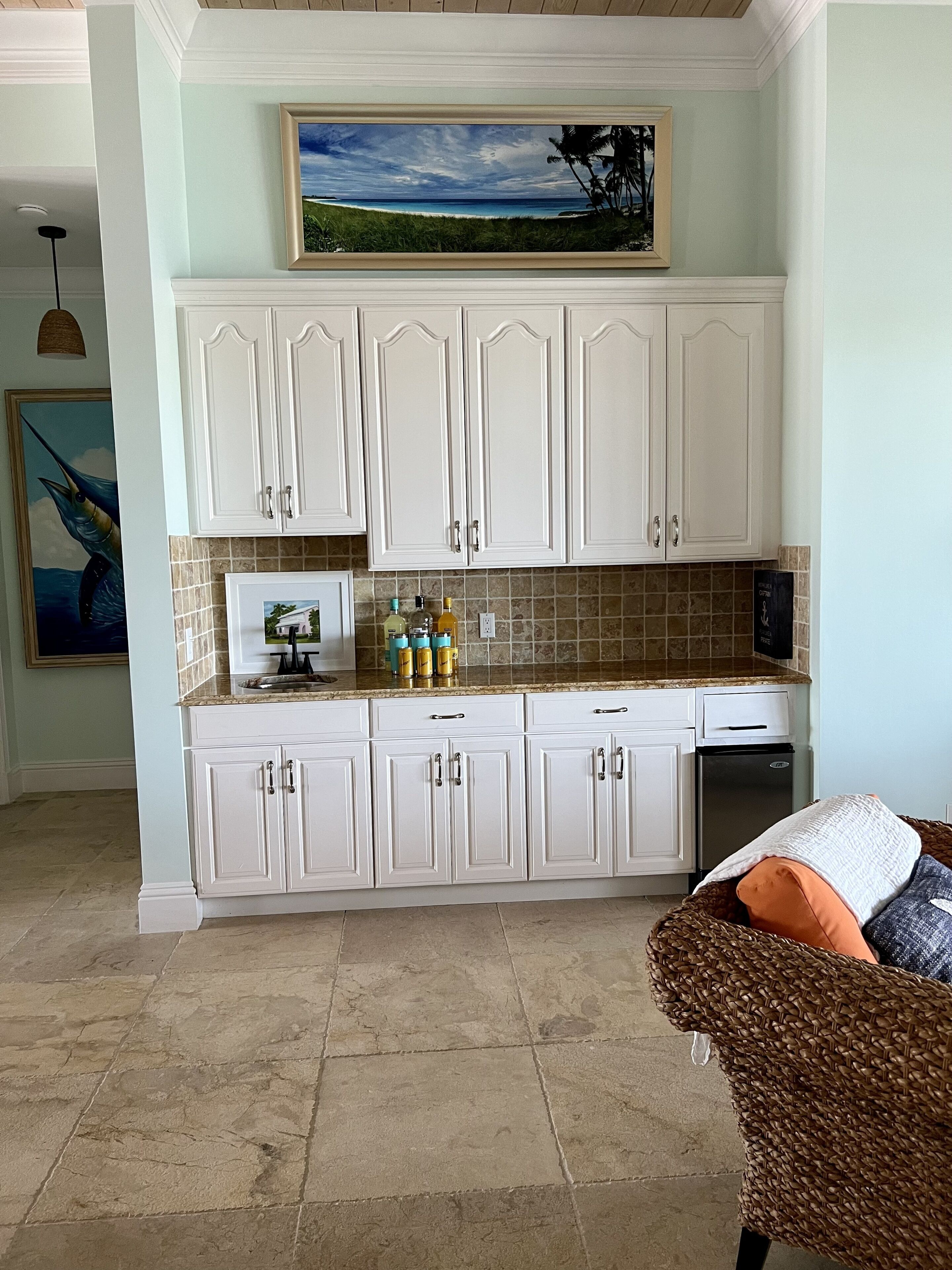 A kitchen with white cabinets, a granite countertop, and a painting above the cabinets.