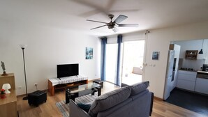 A modern living room with a sofa, TV, and a ceiling fan. - Appt "chrisanne" 3 T2 Grande Terrasse à St Gilles (Saint Paul)