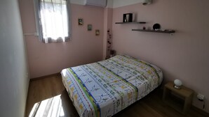 A bedroom with a bed, a ceiling fan, a window with curtains, and a wall-mounted air conditioner. - Appt "chrisanne" 3 T2 Grande Terrasse à St Gilles (Saint Paul)