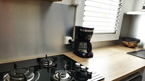 A kitchen with a gas stove, a coffee maker, and a window with blinds. - Appt "chrisanne" 3 T2 Grande Terrasse à St Gilles (Saint Paul)