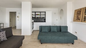 Una sala moderna con un sofá y un sofá verde, una cocina al fondo y una puerta que da a otra habitación.