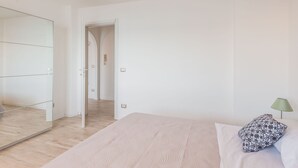 Un dormitorio con un espejo grande, una cama con almohadones estampados y una lámpara verde.