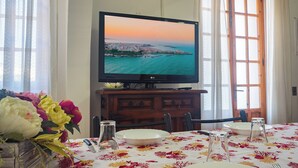 Ein Essbereich mit einem Tisch für zwei Personen, einem Fernseher, der eine schöne Aussicht zeigt, und einer Tischdecke mit Blumenmuster.