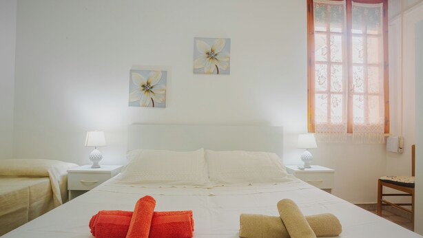 Ein Hotelzimmer mit einem großen Bett, zwei Nachttischen mit Lampen, einem Fenster mit Spitzenvorhängen und zwei an der Wand hängenden Blumenbildern.