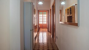 Ein schmaler Korridor mit Fliesenboden, Holztüren und einem Kühlschrank links.