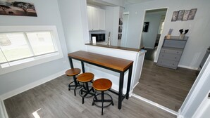 A modern kitchen with a wooden bar and stools, white cabinetry, and a grey floor.
