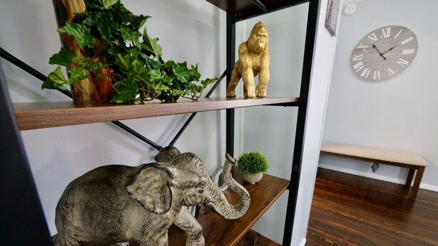 A wooden shelf with a clock, a small plant, and a decorative elephant figurine.