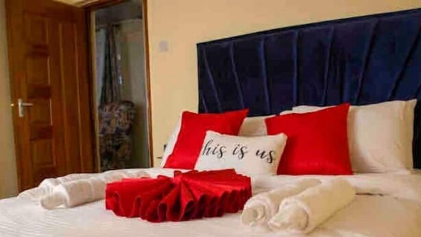 Ein ordentlich gemachtes Bett mit roten und weißen Kissen, einer roten Decke und aufgerollten weißen Handtüchern.