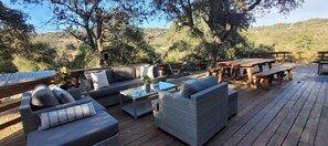 Relax on the deck with sofas and benches, surrounded by trees and a scenic hilly landscape.