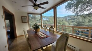 Ein Essbereich mit Holztisch, Stühlen, einem Deckenventilator und Blick auf eine bewaldete Landschaft durch große Fenster.