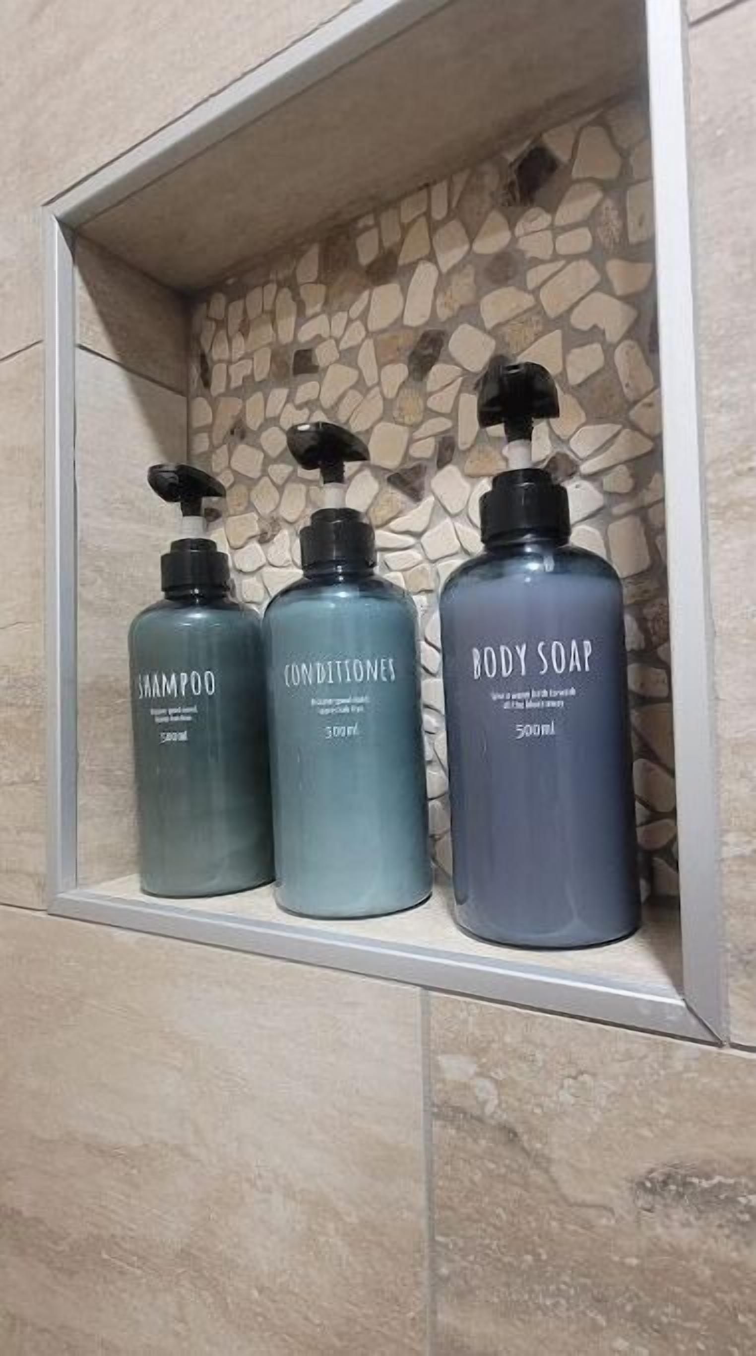 Three bottles of shampoo, conditioner, and body soap in a bathroom shelf.