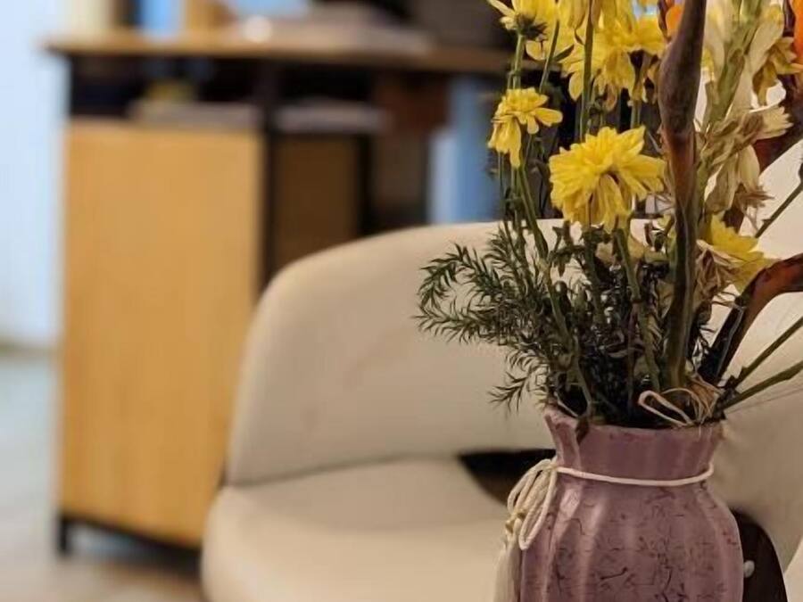 A living room with a purple vase of yellow flowers on a round wooden table.