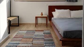 A bedroom with a bed, a window, a small table with a vase, and a patterned rug.