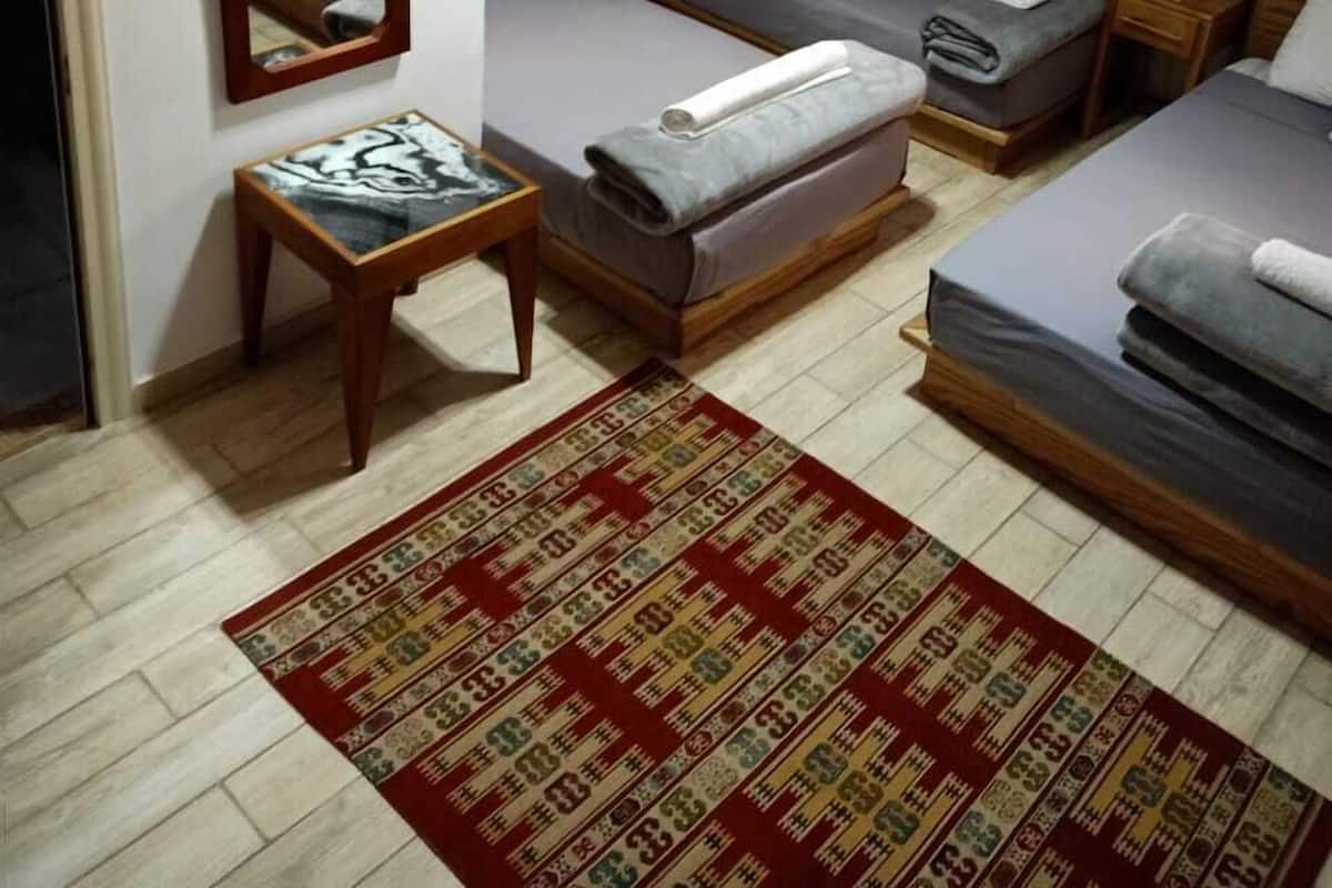A small, neatly arranged bedroom with a bed, a side table, a mirror, and a patterned rug.