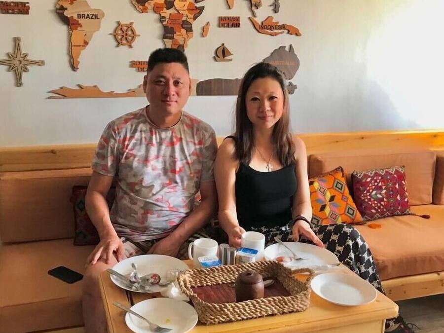Una pareja sentada en un sofá frente a una mesa de madera, sosteniendo una bandeja con un plato, una taza y una cesta.