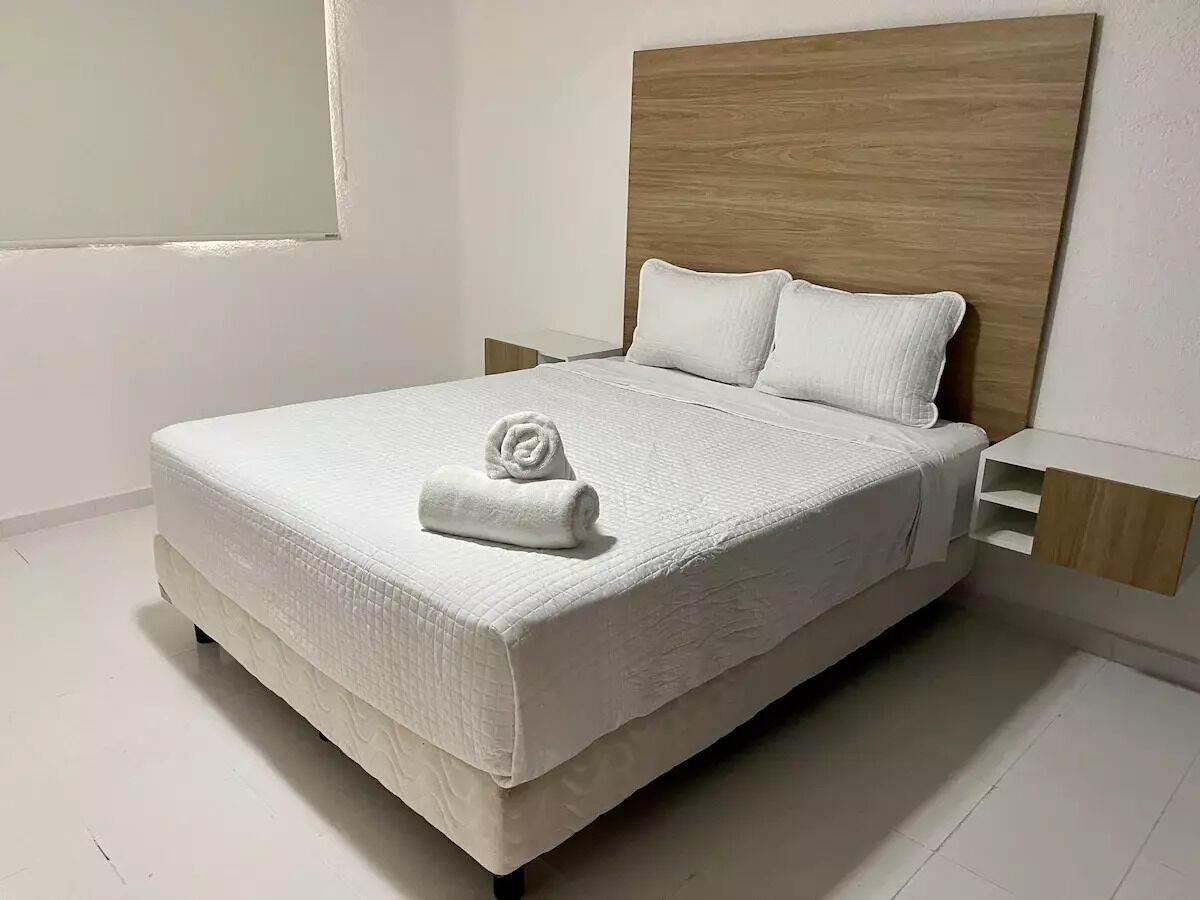 A neatly made bed with a wooden headboard, a white pillow, and a rolled towel on the bed.