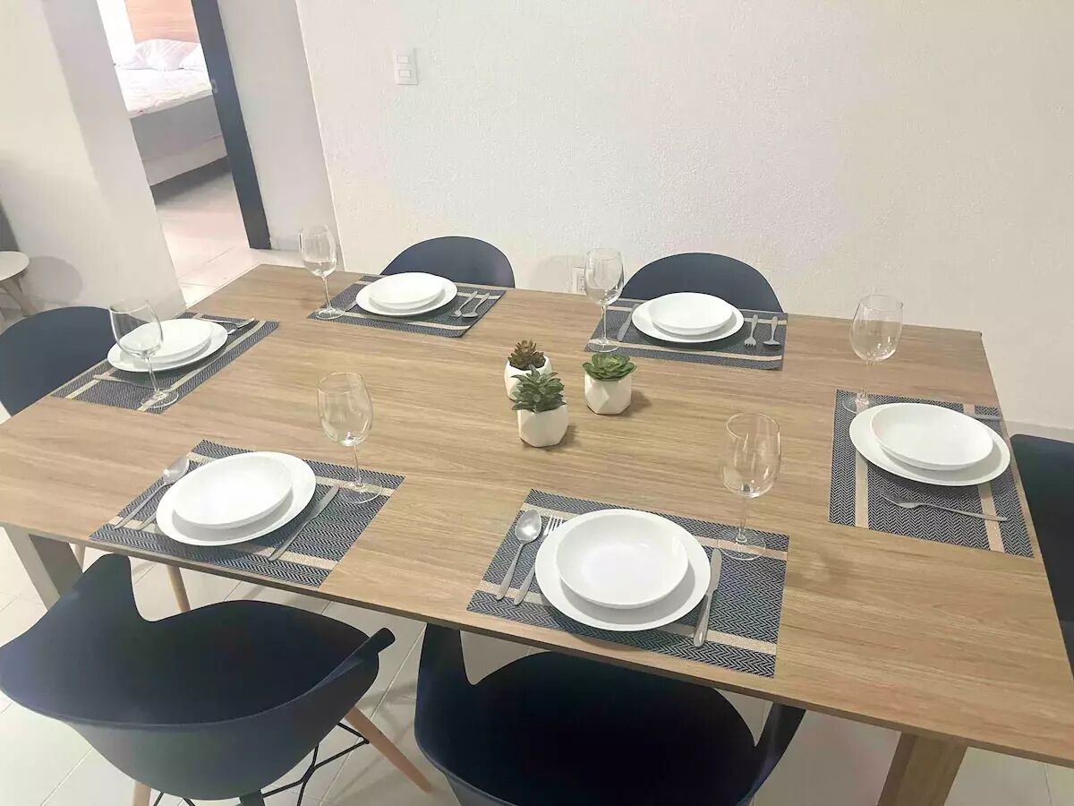 A dining table set for six with placemats, plates, cutlery, and glasses.
