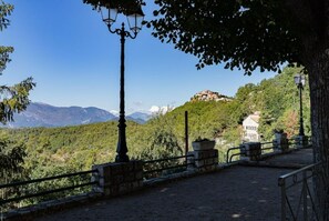 Un vialetto lastricato con ringhiere in pietra, un lampione e vista su un paesaggio montuoso con un edificio sullo sfondo.