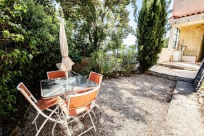 Una terrazza esterna con tavolo e sedie in vetro, circondata da ghiaia e piante.