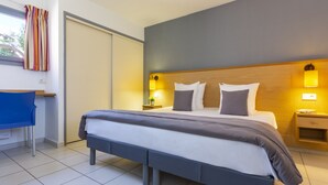 Una habitación de hotel moderna con una cama grande, mesitas de noche con lámparas, un escritorio con silla y vistas al exterior a través de una ventana.