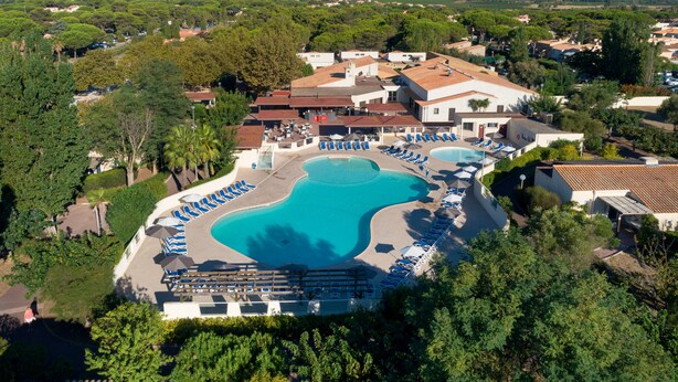 Vista aérea de un complejo turístico con una gran piscina, varias zonas de descanso y un paisaje montañoso de fondo.