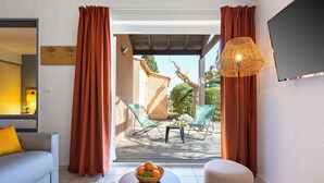 Una sala moderna con un sofá, una mesa baja con un libro y un frutero, un televisor, y un balcón con sillas y una mesa.