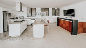 Een moderne keuken met witte kasten, een centraal eiland en een eethoek met stoelen.