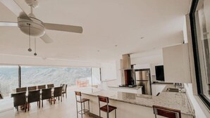 Een moderne keuken met een groot eiland, barstoelen en een plafondventilator.