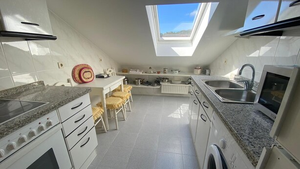A compact kitchen with a skylight, white cabinets, a granite countertop, a washing machine, and a dining area with a table and chairs.