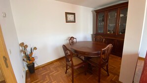 A dining area with a wooden table and chairs, a cabinet with glass doors, and a potted plant with dried flowers.