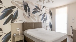 Ein modernes Schlafzimmer mit einem großen Bett, einem Nachttisch, einem Schreibtisch und einer Wand mit Blättermotiv.