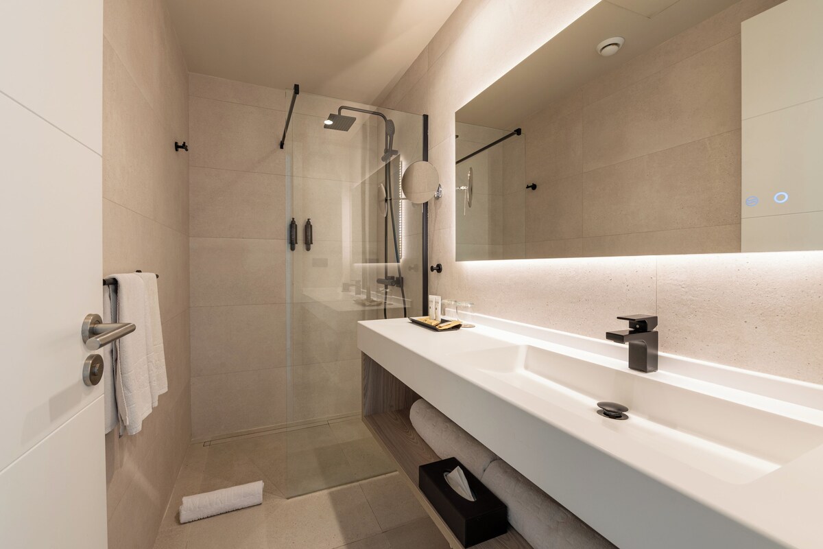 A modern bathroom with a glass-enclosed shower, a white vanity with a mirror, and a towel rack.