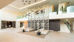 A spacious lobby with a modern design, featuring a seating area with sofas and a coffee table, a staircase, and a decorative wall with geometric patterns.