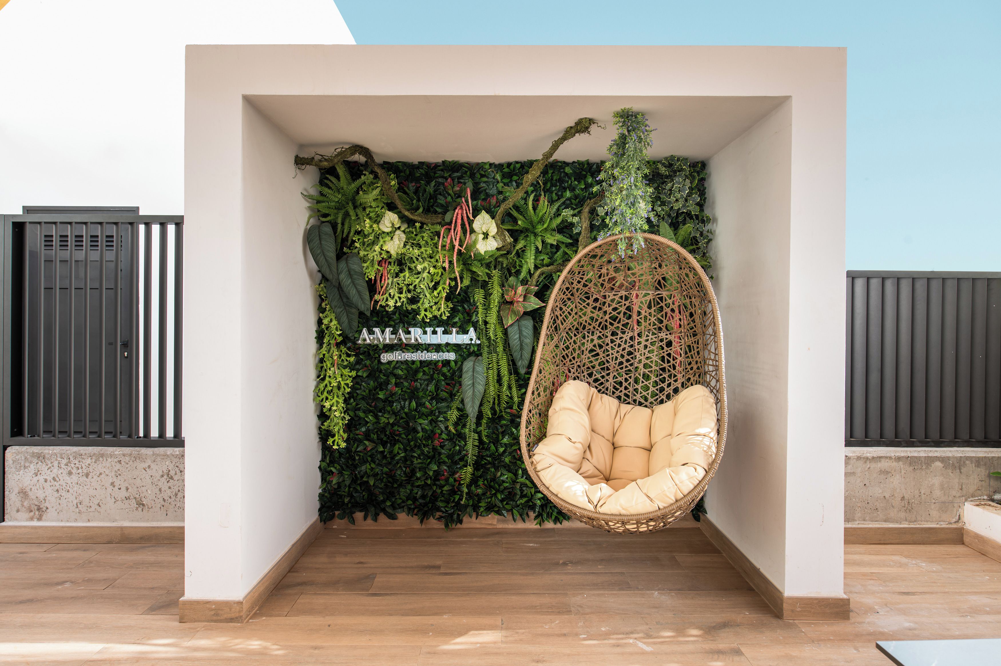 A hanging chair in a corner with a wall of green foliage and a sign that reads 'AMARITA golf residences'.
