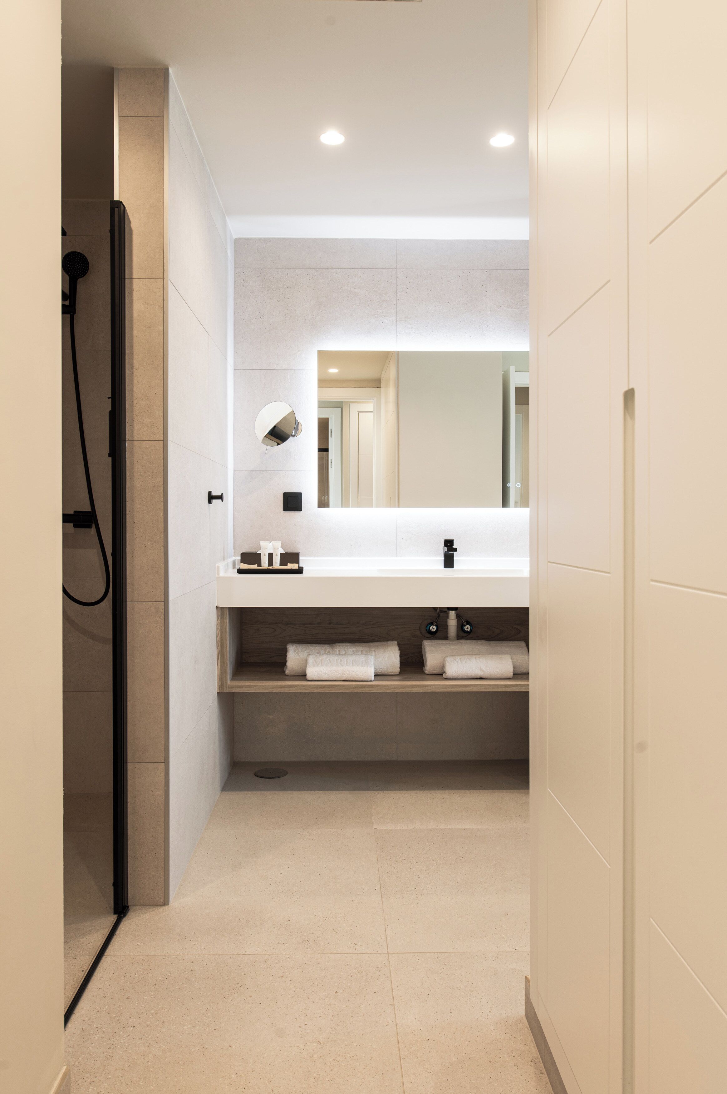 Un baño moderno con ducha, lavamanos con espejo y toallas ordenadas en un estante.
