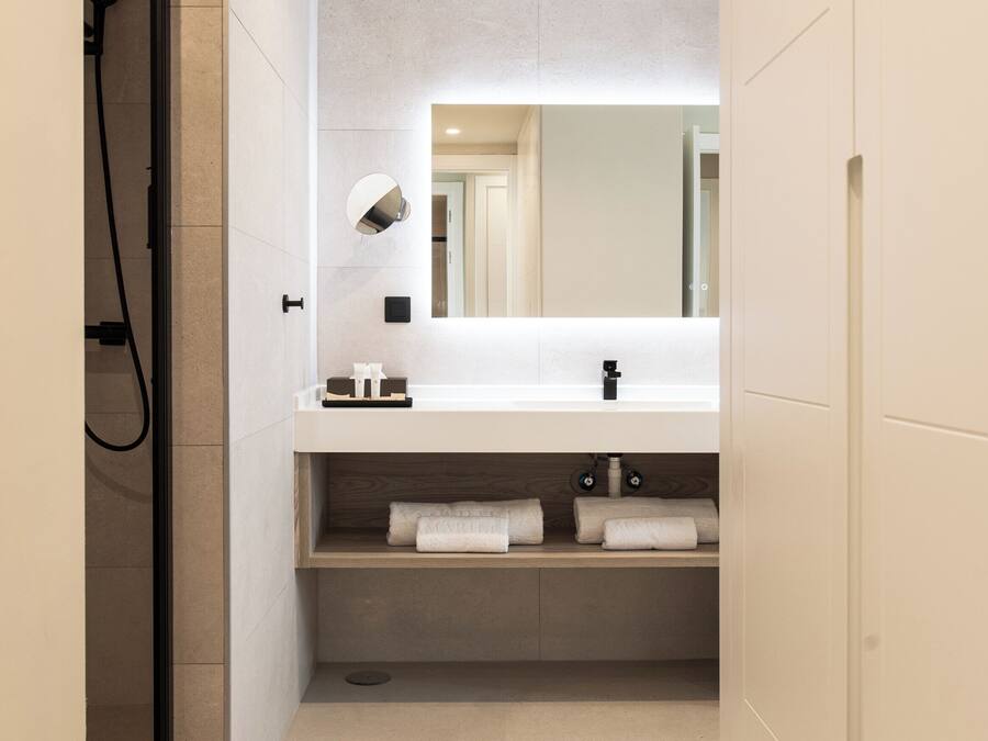 Un baño moderno con ducha, lavamanos con espejo y toallas ordenadas en un estante.
