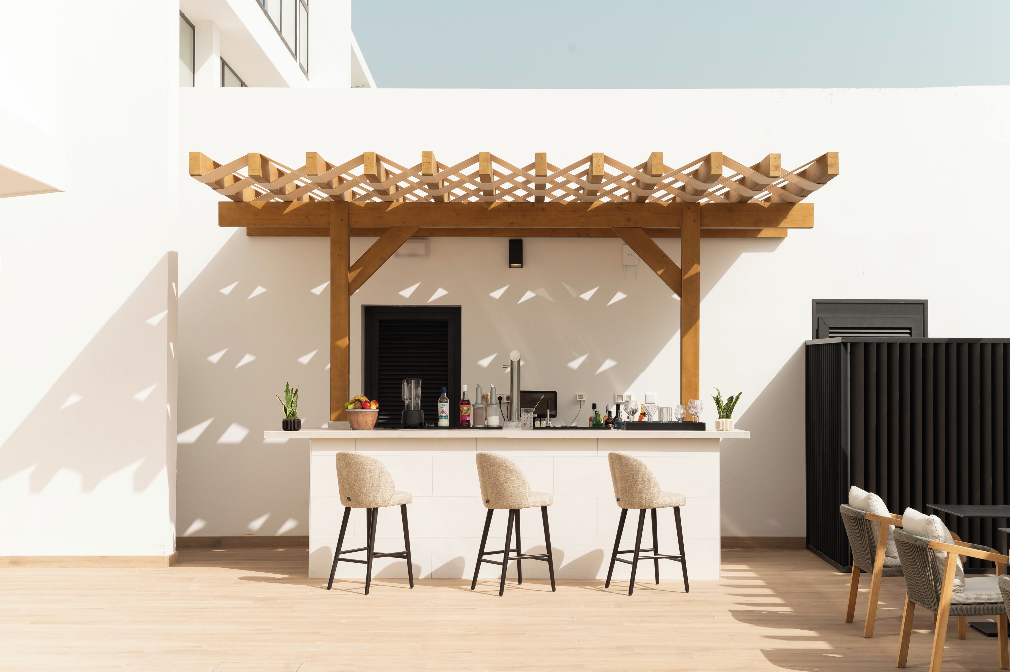 A bar area with a wooden pergola, a counter with bar stools, and a seating area with chairs.