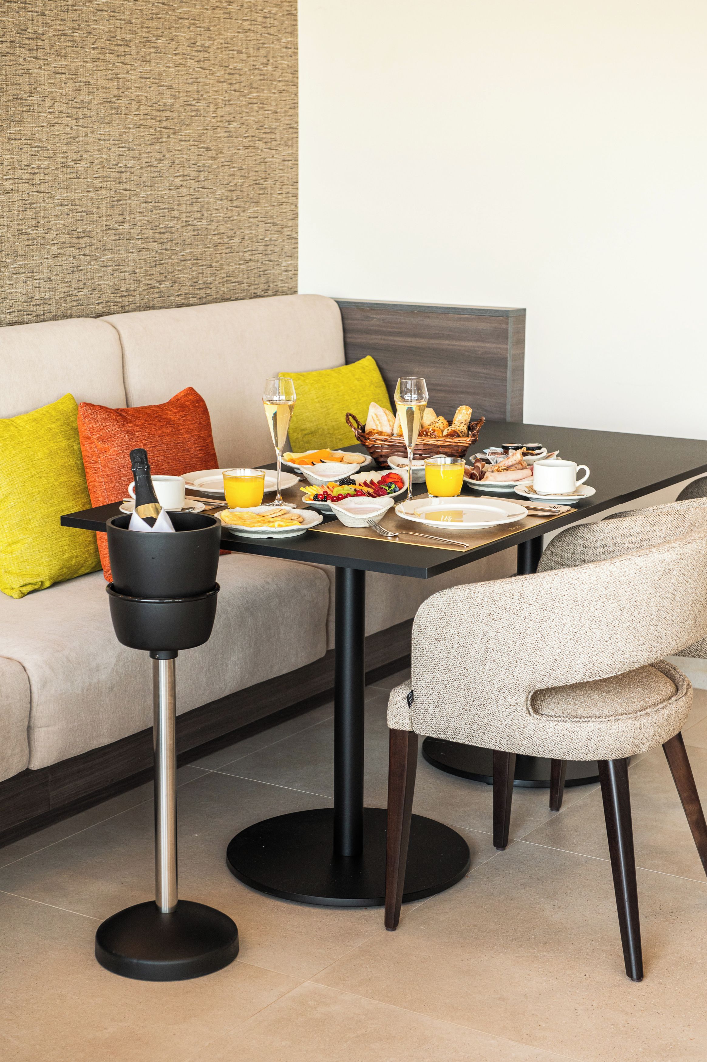 A dining table set with plates, glasses, and a bottle of champagne, placed in a modern room with a sofa and a round table.