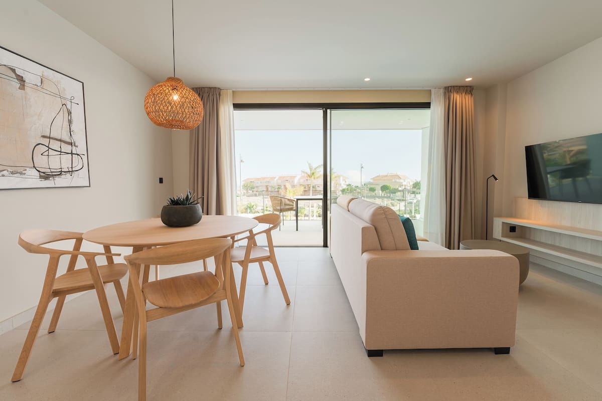 Un salon moderne comprenant un canapé, une table à manger avec des chaises, un luminaire suspendu et un téléviseur posé sur un meuble.