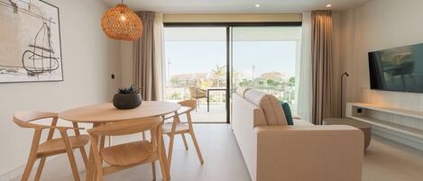 Una sala de estar moderna con un sofá, una mesa de comedor con sillas, una lámpara colgante y un televisor sobre un mueble.