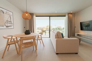 A modern living room with a sofa, a dining table with chairs, a hanging light fixture, and a TV on a stand. - Amarilla Golf Residences (San Miguel de Abona)