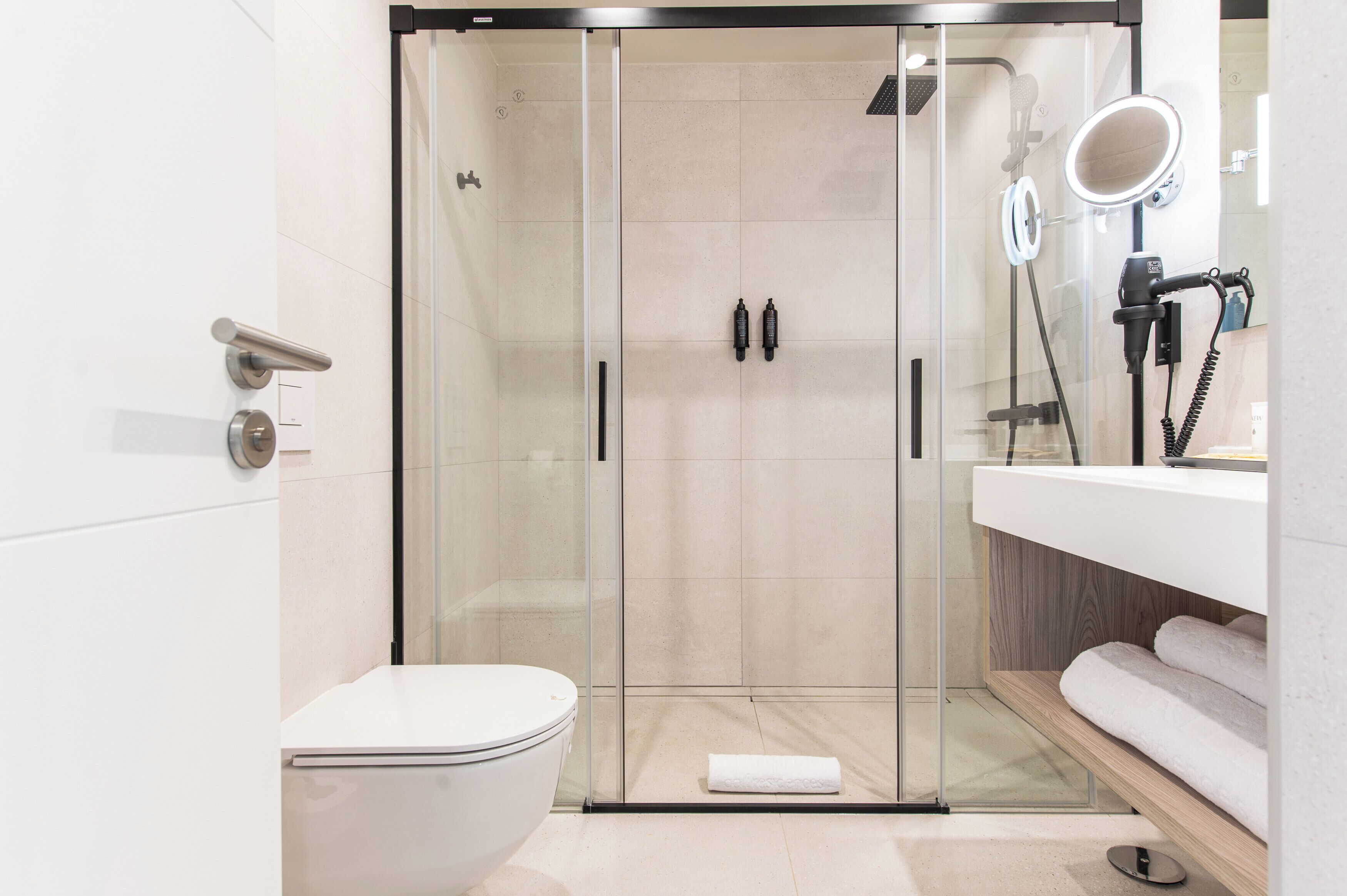 Une salle de bain moderne avec une douche à parois de verre, des toilettes blanches, un meuble-lavabo avec un miroir et un porte-serviettes.