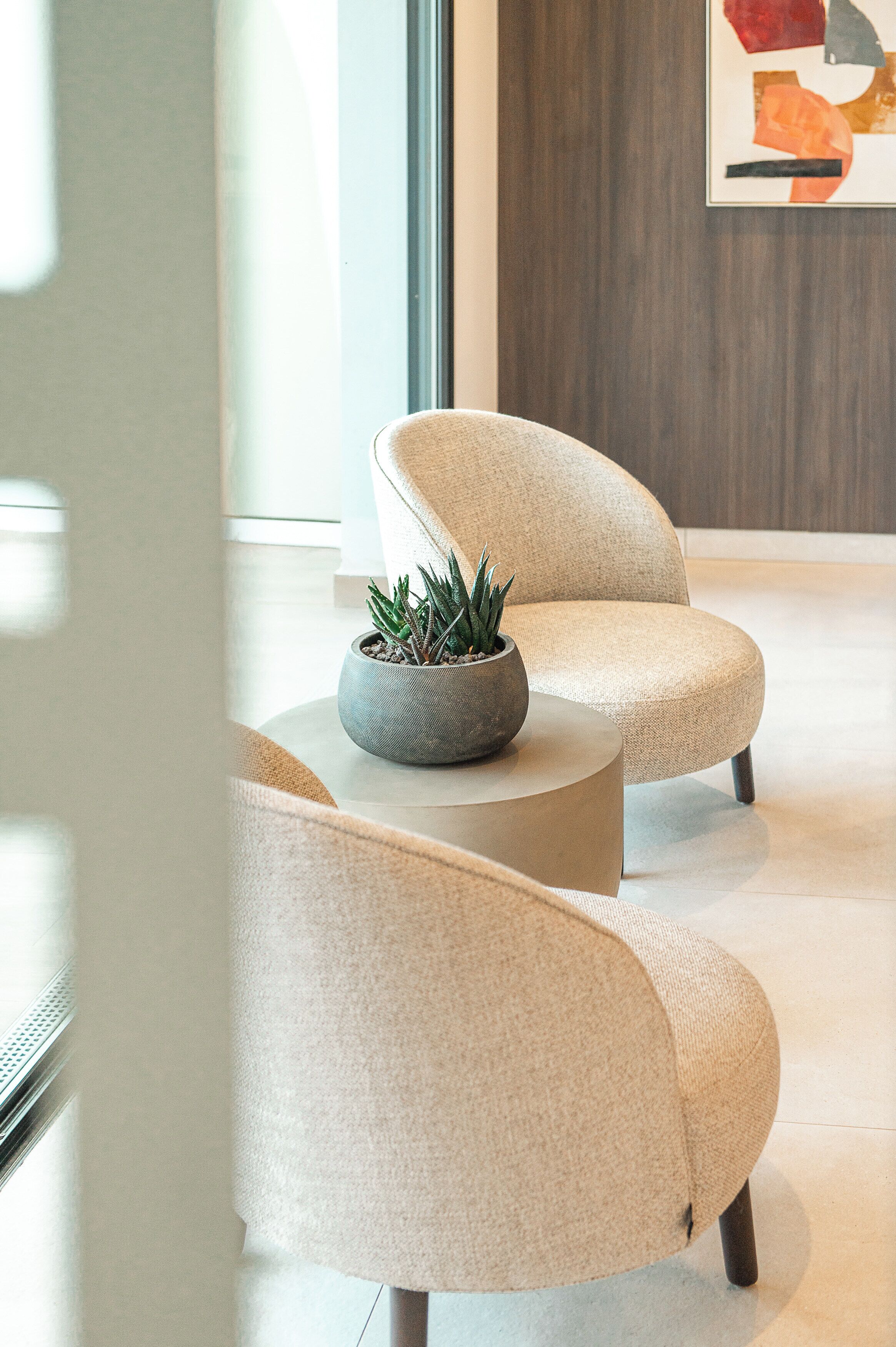 En moderne lobby med to beige lænestole, et rundt sofabord og en potteplante.