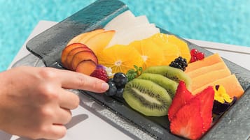A fruit platter with various fruits and berries on a table by a pool.