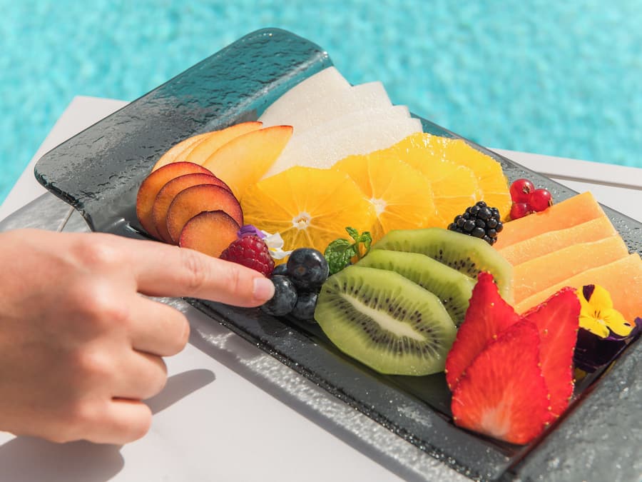 A fruit platter with various fruits and berries on a table by a pool.