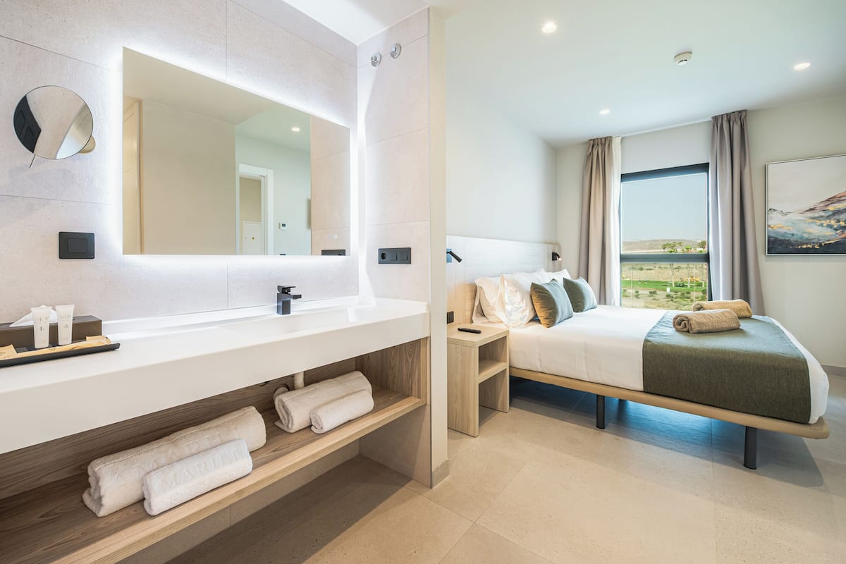 Une chambre d’hôtel moderne dotée d’un grand miroir, d’une coiffeuse en bois, d’un lit avec vue et d’une petite table de chevet.