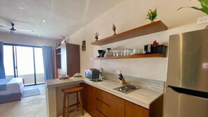 A modern kitchen with wooden cabinets, a stainless steel refrigerator, and a built-in oven. There is a bar stool and a small island with a sink. - Lovely Loft In Veleta (Tulum)