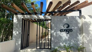 A gated entrance with a pergola overhead, a concrete wall with a logo, and potted plants at the base. - Lovely Loft In Veleta (Tulum)