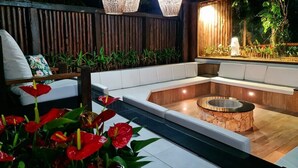Un espacio exterior moderno con una chimenea de piedra, asientos acolchados e iluminación decorativa.