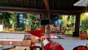 Un área de estar al aire libre con una pantalla de televisión, rodeada de abundante vegetación y plantas.